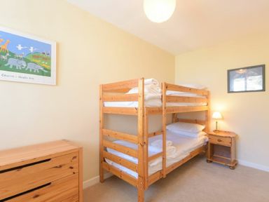 A bedroom with a wooden bunk bed a wooden dresser a bedside table with a lamp and framed pictures on the walls at The Boathouse (Alnmouth) in Alnmouth