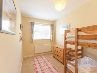 A bedroom with wooden bunk beds a wooden dresser a window with curtains and a striped rug on the floor at The Boathouse (Alnmouth) in Alnmouth
