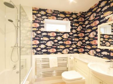 A bathroom with a shower bathtub toilet sink and fish patterned wallpaper at The Boathouse (Alnmouth) in Alnmouth