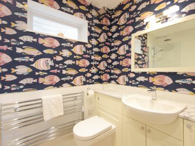 A bathroom with fish patterned wallpaper a white toilet and sink a large mirror and a towel rack at The Boathouse (Alnmouth) in Alnmouth