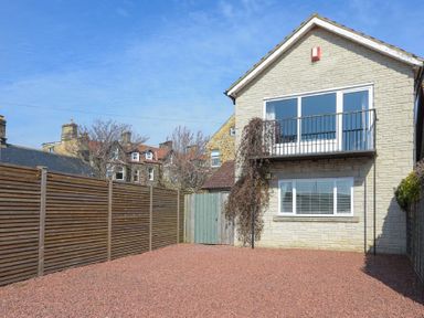 A fenced backyard with gravel ground and a two-story stone house with a balcony at The Boathouse in Alnmouth