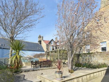 An outdoor garden with trees wooden table and chairs and stone walls at The Boathouse in Alnmouth