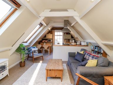 A living room with a gray sofa wooden coffee table and armchair facing a kitchen and dining area at Coach House (Alnmouth) in Alnmouth