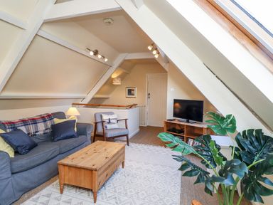 A living room with a sofa armchair wooden coffee table and television at Coach House Alnmouth