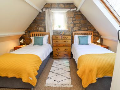 A bedroom with two single beds with yellow blankets and a wooden chest of drawers between them at Coach House (Alnmouth) in Alnmouth