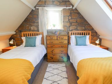 A bedroom with two single beds with yellow throws and blue pillows a wooden chest of drawers and a small window at Coach House (Alnmouth) in Alnmouth