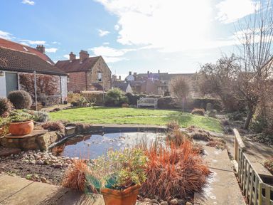 A garden with a pond grass and trees near houses at Coach House in Alnmouth