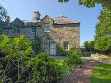 A stone house with a white door and windows with a path and garden in front at Avocet Cottage in Bamburgh