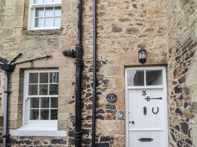 A stone exterior wall with two windows a white door with number 3 and black drainpipes at Avocet Cottage in Bamburgh