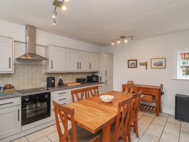 A kitchen with wooden dining table and chairs white cabinets and appliances at Avocet Cottage in Bamburgh