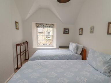 A bedroom with two single beds beside a window with floral blinds and framed pictures on the walls at Avocet Cottage in Bamburgh