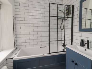 A bathroom with a bathtub shower combination and a sink with a mirror at Avocet Cottage in Bamburgh
