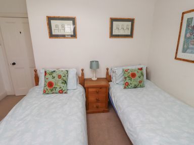 A bedroom with two single beds a wooden nightstand and framed pictures on the walls at Avocet Cottage in Bamburgh