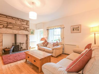 A living room with two sofas a wooden coffee table a stone fireplace and a window at Dunlin Cottage in Bamburgh