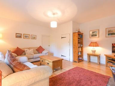 A living room with beige sofas wooden coffee table wooden bookshelf and red rug at Dunlin Cottage in Bamburgh