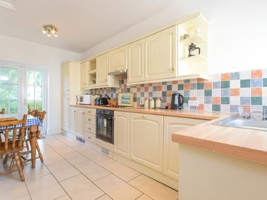 A kitchen with cream cabinets tiled backsplash oven and wooden dining table at Dunlin Cottage in Bamburgh