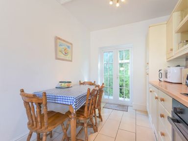 A kitchen with wooden chairs and a table with a blue checkered tablecloth next to glass doors at Dunlin Cottage in Bamburgh