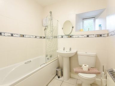 A bathroom with a bathtub shower sink toilet and small window at Dunlin Cottage in Bamburgh