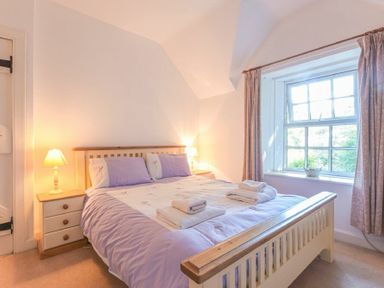 A bedroom with a double bed, bedside tables with lamps, folded towels on the bed, and a window with curtains at Dunlin Cottage in Bamburgh