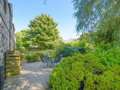An outdoor patio with a table and four chairs surrounded by bushes and trees at Dunlin Cottage in Bamburgh