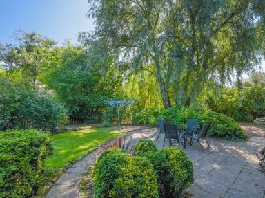 A garden patio with a table and four chairs surrounded by trees and bushes at Dunlin Cottage in Bamburgh