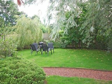 A garden with green grass a table with four chairs and surrounding trees at Dunlin Cottage in Bamburgh