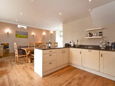 A kitchen and dining area with wooden chairs a table and cabinets at High Tide in Newton-by-the-Sea