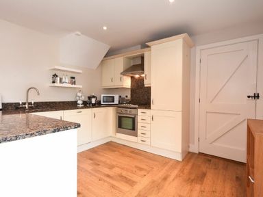 A kitchen with white cabinets a microwave an oven and a wooden floor at High Tide in Newton-by-the-Sea
