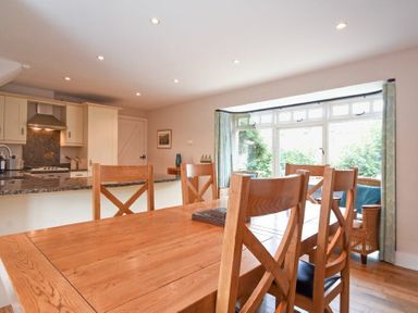 A dining area with wooden chairs and table next to a kitchen with an island and large windows at High Tide in Newton-by-the-Sea