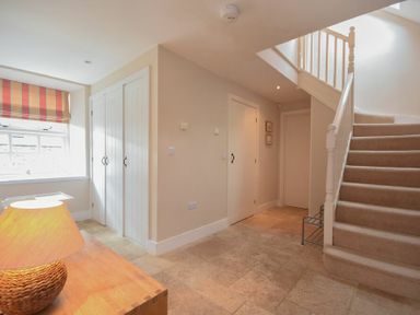 A hallway with stairs and closed doors next to a window and a wooden table with a lamp at High Tide in Newton-by-the-Sea