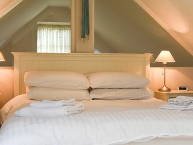A bedroom with a bed white pillows folded towels bedside lamps and a window reflected in a mirror at High Tide in Newton-by-the-Sea