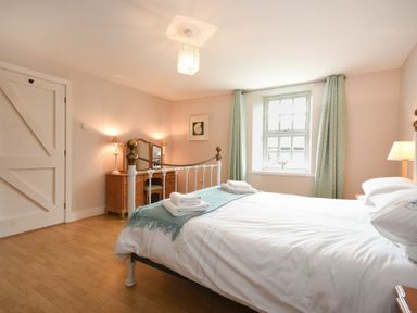 A bedroom with a bed a dressing table lamps and a window with curtains at High Tide in Newton-by-the-Sea