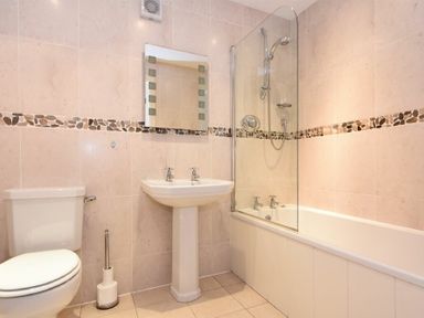 A bathroom with a toilet pedestal sink mirror and bathtub with shower at High Tide in Newton-by-the-Sea