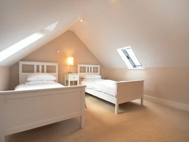 A bedroom with two single beds a nightstand and a lamp under slanted ceilings at High Tide in Newton-by-the-Sea