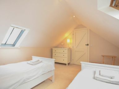 A bedroom with two single beds a dresser a door a skylight window and a small table at High Tide in Newton-by-the-Sea