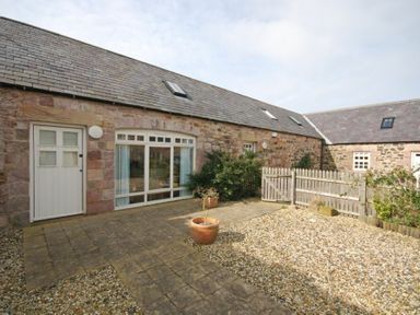 A stone exterior courtyard with a white door large window potted plants and a wooden gate at High Tide in Newton-by-the-Sea