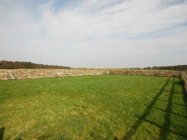 A grassy field enclosed by low stone walls and a wooden fence at High Tide in Newton-by-the-Sea