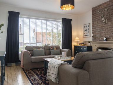 A living room with two sofas a coffee table a sideboard a lamp and a brick fireplace at Sea Croft in Beadnell