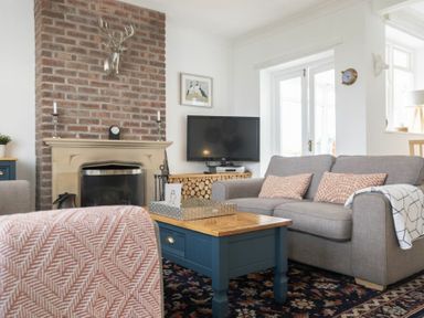 A living room with a brick fireplace a gray sofa a blue coffee table and a television at Sea Croft in Beadnell