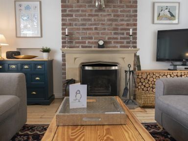 A living room with a fireplace surrounded by brick and two gray sofas at Sea Croft in Beadnell