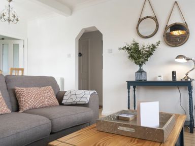 A living room with a grey sofa cushions a wooden coffee table and a blue console table with a lamp and plant at Sea Croft in Beadnell