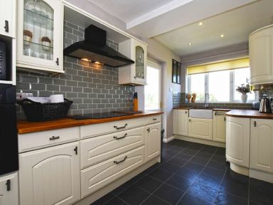 A kitchen with wooden countertops white cabinets a black stove and a window above the sink at Sea Croft in Beadnell