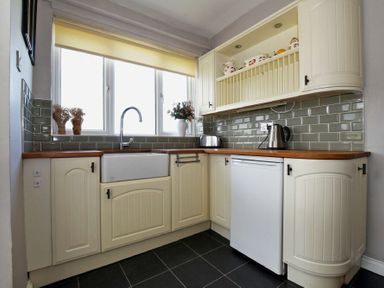 A kitchen with cream cabinets a white sink a kettle and toaster on wooden countertops at Sea Croft in Beadnell