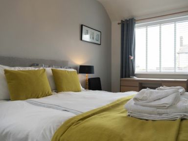 A bedroom with a bed with green pillows and blanket a lamp and a desk by a window at Sea Croft in Beadnell