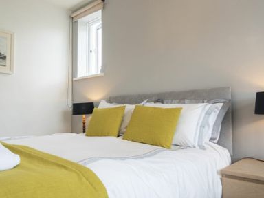 A bedroom with a bed with green cushions a green throw and bedside tables with lamps at Sea Croft in Beadnell