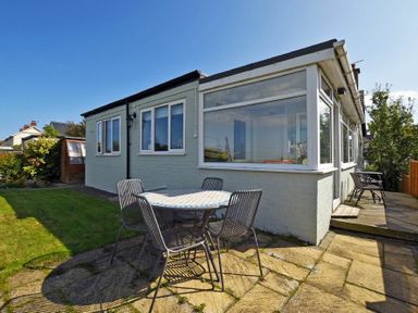 An outdoor patio area with a round table and four chairs next to a white building with large windows at Sea Croft in Beadnell