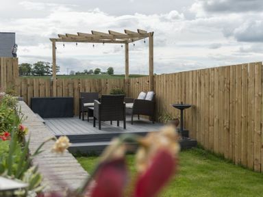 A wooden deck with outdoor furniture and a pergola surrounded by a wooden fence at Sea Croft in Beadnell