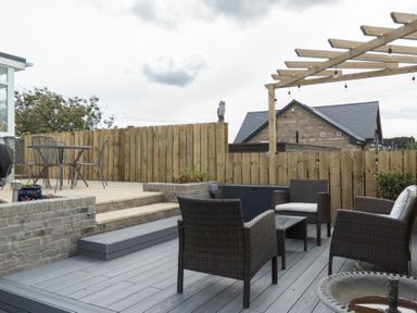 An outdoor patio with wicker chairs a wooden pergola string lights and a dining table on a raised deck at Sea Croft in Beadnell