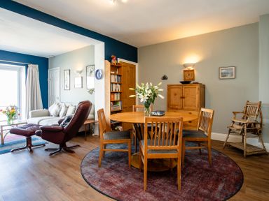 A dining area with a round wooden table and chairs and a living area with armchairs and a sofa at Old Coastguard Cottages in Amble