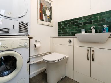 A bathroom with washing machine dryer toilet sink and green tiled backsplash at Old Coastguard Cottages in Amble